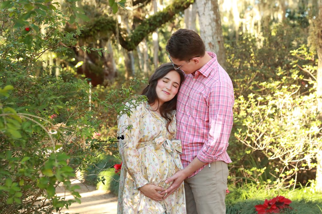 Mom-to-be in a flowing gown posing among lush greenery during a park maternity photoshoot by Katerina Krjanina.