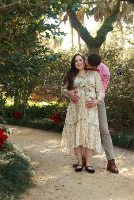 Mom-to-be in a flowing gown posing among lush greenery during a park maternity photoshoot by Katerina Krjanina.